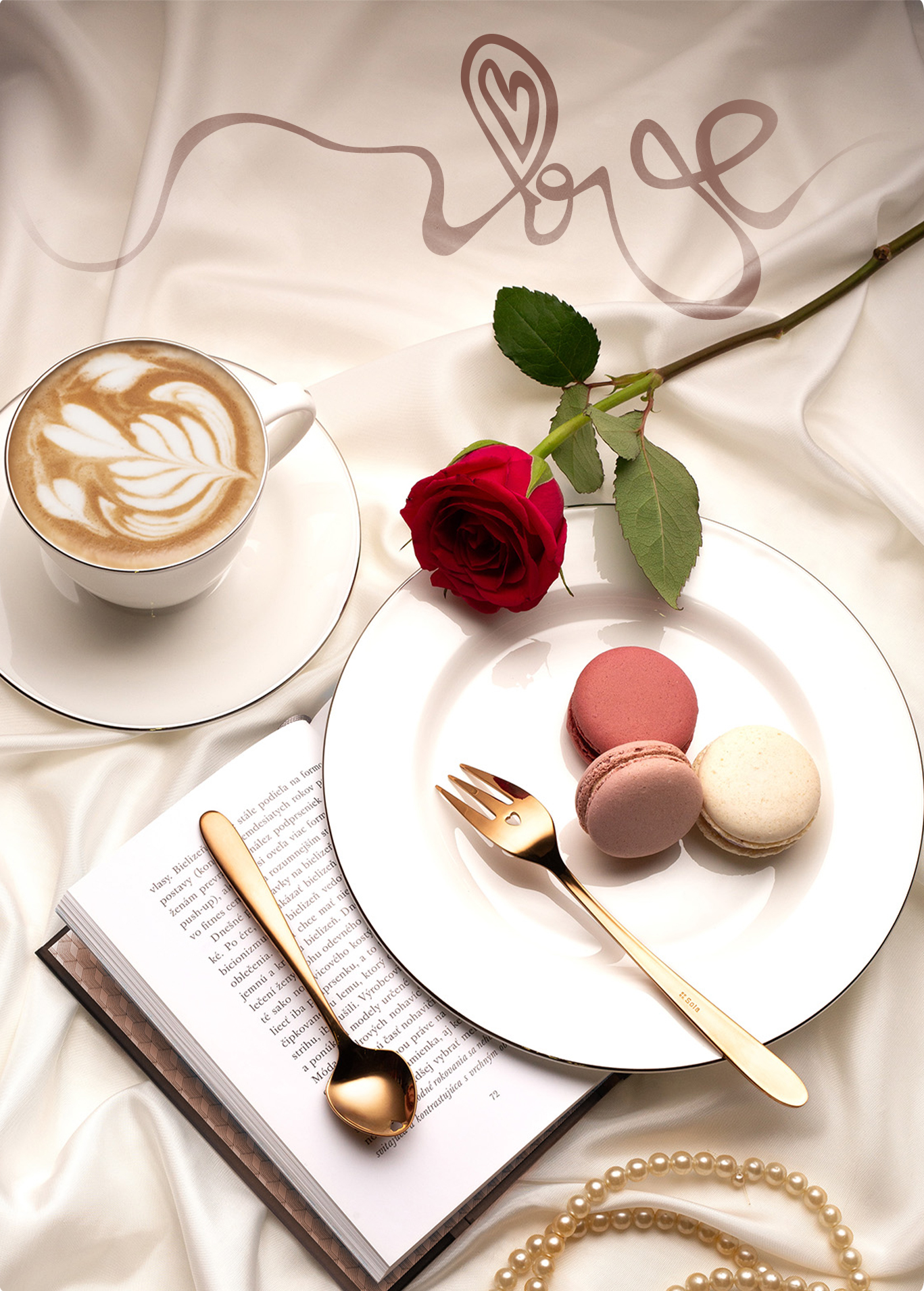 O ceașcă de cafea, un trandafir roșu, macarons, o carte și tacâmuri aurii sunt așezate pe o țesătură albă din satin 