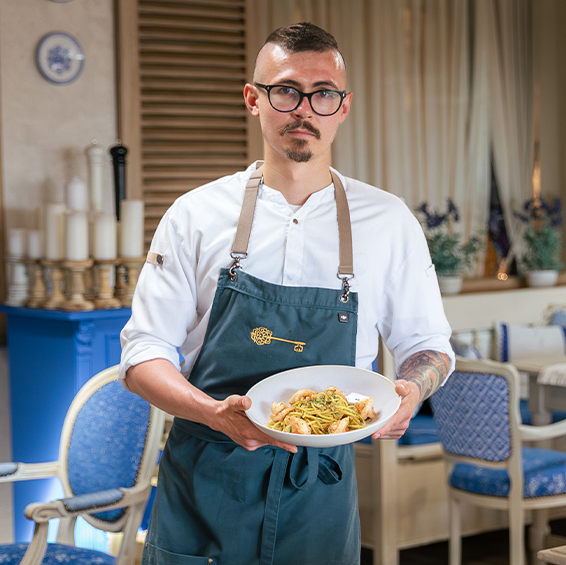 Bucătarul-șef ține o farfurie cu spaghete și creveți în interiorul restaurantului 