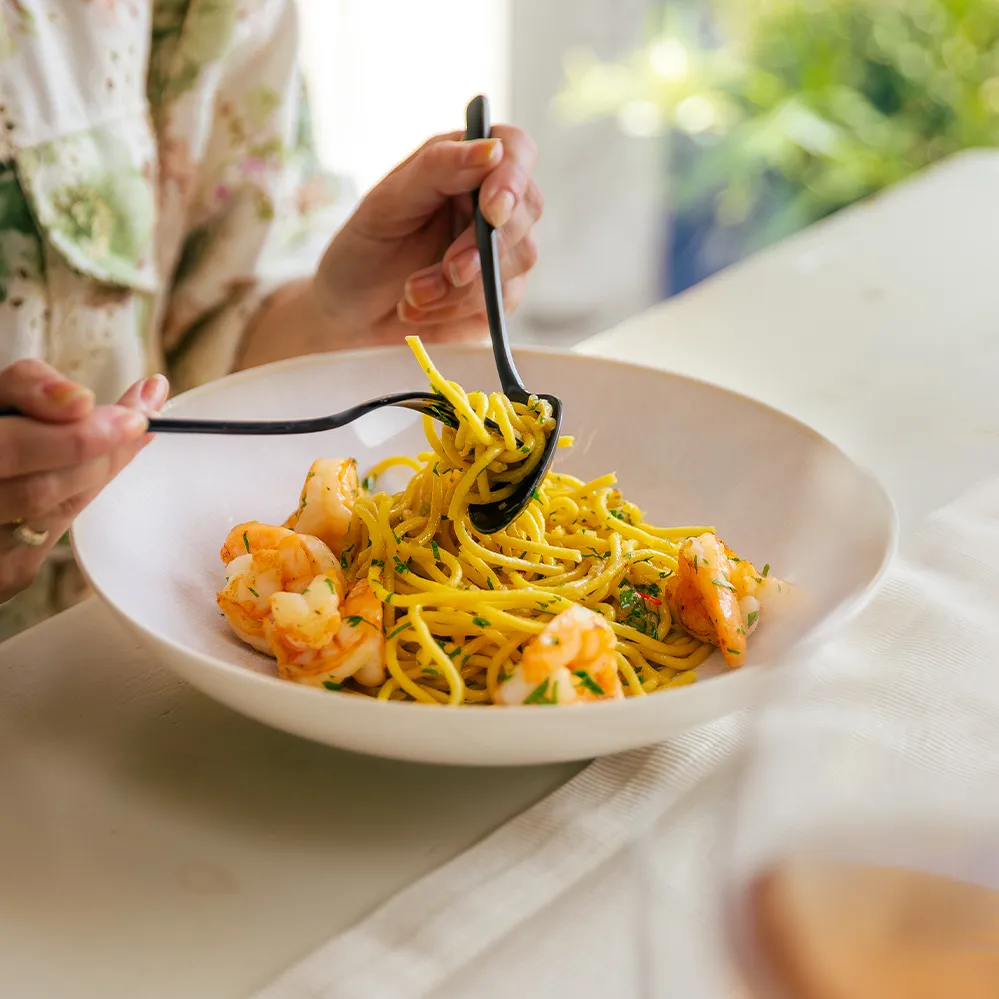 Spaghete cu creveți într-un bol bej, luate cu furculița și lingura